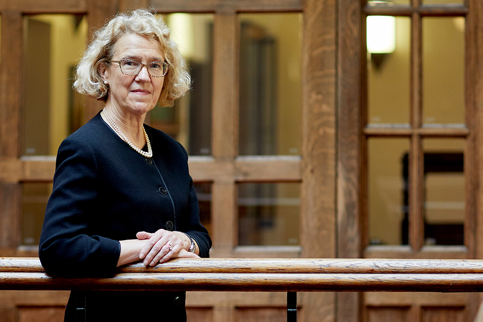 The Right Honourable Lady Justice Thirlwall stands in a courtroom setting, with wood-framed doors and windows visible behind her.