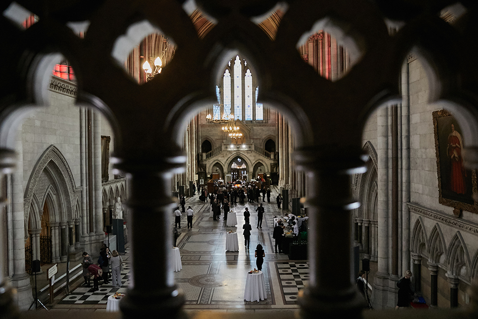 A view of the people mingling at the event in the Royal Courts of Justice, taken from a balcony through an ornate, arched balustrade.